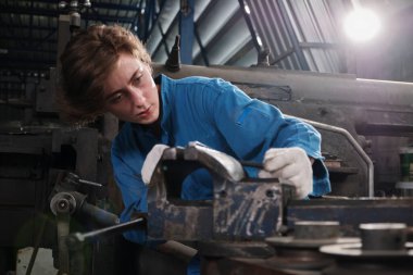 Profesyonel bir kadın mühendis güvenlik üniforması içinde çalışıyor. Metal işçiliği hassas aletleri, mekanik torna makineleri ve çelik fabrikasında yedek parça atölyesi var..