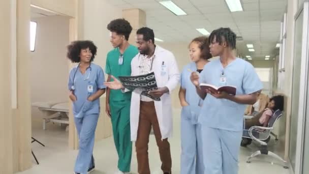 一组从业人员 专业的非洲裔美国男医生与医科学生一起在医院的一个诊所里散步和讨论诊断用的X光片 墙上的泰文意思是 检查室 — 图库视频影像