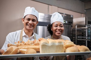 Beyaz üniformalı profesyonel şeflerin portresi kameraya neşeli bir gülümsemeyle bakıyor ve mutfakta bir tepsi ekmekle gurur duyuyor. Pastane yemekleri ve taze günlük fırın işlerinden bir arkadaş ve ortak..