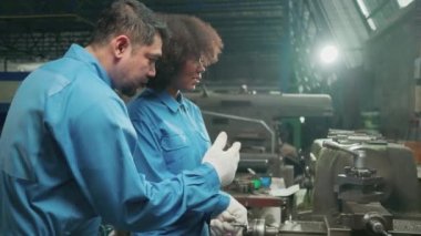 İki profesyonel endüstri mühendisi güvenlik üniforması içinde çalışıyor. Metal işçiliği hassas aletleri, mekanik torna makineleri ve çelik fabrikasında yedek parça atölyesi var..