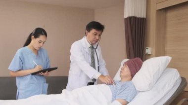 Üniformalı profesyonel doktorlar Asyalı erkek hastayı steteskopla kontrol ediyor, hastane koğuşundaki yatağında ilaç tedavisi görüyor, tıbbi klinik, kanser muayenesi....