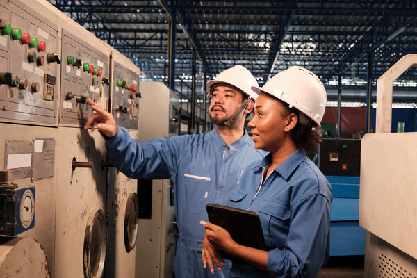 Профессиональный промышленный инженер-партнер в жестких шляпах и униформе безопасности инспектировать панель управления машины, техническое обслуживание с планшетом на заводе механического производства, электротехническое обслуживание занятости.