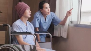 Üniformalı genç Asyalı kadın terapist, hastane yatağında kemoterapi gördükten sonra iyileşme ve motivasyon için tekerlekli sandalyeli erkek hastayı teşvik ediyor..