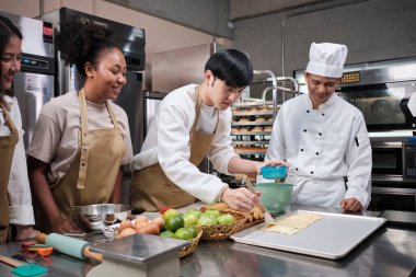 Mutfak kursu, üniformalı kıdemli aşçı genç aşçılık sınıfı öğrencilerine ders veriyor, yumurta kremalı hamur işleri yapıyor, fırın yemekleri için malzemeler hazırlıyor, paslanmaz çelik mutfakta meyveli turtalar hazırlıyor..