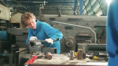 Profesyonel bir kadın mühendis güvenlik üniforması içinde çalışıyor. Metal işçiliği hassas aletleri, mekanik torna makineleri ve çelik fabrikasında yedek parça atölyesi var..