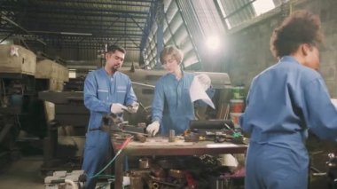 Güvenlik üniforması giyen iki profesyonel endüstri çalışanı ve mühendis ortakları metal iş araçlarıyla çalıştılar, torna makinelerinin mekanik çizimini tartıştılar ve imalathanede atölye çalışmalarını tartıştılar..