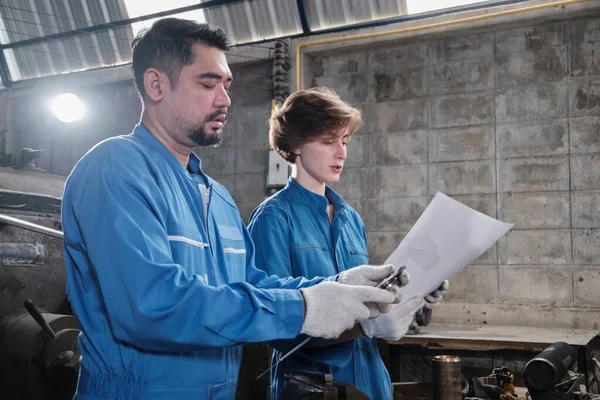 Two professional industry workers teams in safety uniforms and engineers' partners worked with metalwork tools, discussed mechanical drawing for lathe machines, and workshop in manufacturing factory.