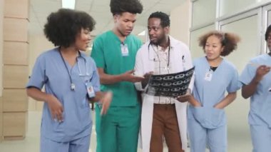 Bir grup pratisyen, genç tıp öğrencileri olan profesyonel Afro-Amerikalı erkek doktor hastanedeki ayakta tedavi kliniğinde röntgen filmlerini tartışmaktan mutlu olurlar..