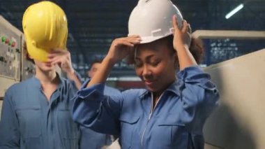 Çok ırklı profesyonel mühendis ekibi işten sonra şapkalarını çıkartıp neşeli gülümsemeler ve endüstriyel üretim fabrikasındaki olumlu ifadelerle kameraya bakıyorlar. Mutlu teknisyenlik görevi..