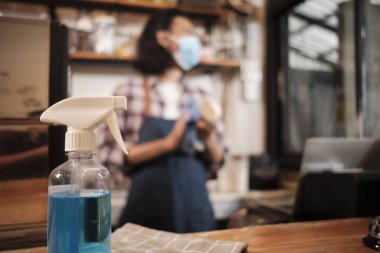 Bir kafede sağlıklı korunma için alkol dezenfektanı, yüz maskeli Asyalı erkek barista dizüstü bilgisayar kullanıyor, COVID19 pandemik karantinasında kahve siparişini bekliyor, bu da küçük işletmeler için ekonomik etki..