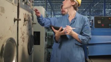 Profesyonel endüstri mühendisi ekipleri başlık ve güvenlik üniformalarıyla makinenin kontrol panelini, mekanik imalat fabrikasında tabletle bakım kontrolünü, elektrik servis işgalini denetliyor..