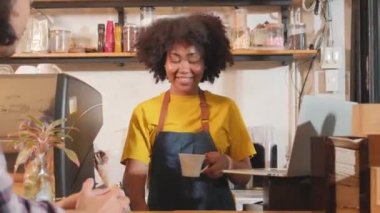 Gündelik önlüklü Afro-Amerikan bayan kafe kahvecisi. Laptopta online müşteri siparişiyle mutlu. Kahve dükkanındaki tezgah barında gülümseyen neşeli çalışmalar..