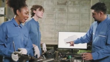 Üç çok ırklı profesyonel endüstri mühendisi güvenlik üniformalı işçiler metal işçiliği işleri bir monitör, torna makineleri ve imalat fabrikasında atölye ile mekanik çizim tartışır.