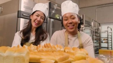 Profesyonel kadın şeflerin portresi üniformalı neşeli bir gülümsemeyle kameraya bakıyor ve mutfakta bir tepsi ekmekle gurur duyuyor. Pastane yemekleri ve taze günlük fırın işlerinden bir arkadaş ve ortak..