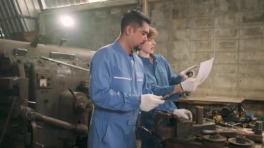 Güvenlik üniforması giyen iki profesyonel endüstri çalışanı ve mühendis ortakları metal iş araçlarıyla çalıştılar, torna makinelerinin mekanik çizimini tartıştılar ve imalathanede atölye çalışmalarını tartıştılar..