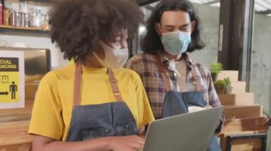 Two young cafe barista partners and entrepreneur work with face mask in coffee shop, waiting for customers order in new normal lifestyle service, SME business impact from COVID19 pandemic quarantine.