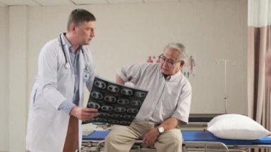 Üniformalı beyaz erkek doktor hastalıkları kontrol ediyor kıdemli hasta, teşhis, hastane koğuşundaki acil serviste röntgen filmini, yaşlılar kliniğini, acılı muayene danışmanını açıklıyor..