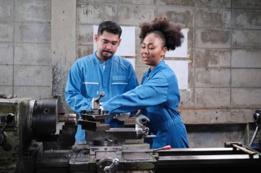 Güvenlik üniforması ve mühendis ortağı olan iki profesyonel endüstri çalışanı hassas metal işçiliği araçlarıyla çalıştı ve fabrikadaki torna atölyesindeki makine atölyesinin mekanik çizimini tartıştılar..