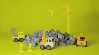 Sarı arka planda stop-motion, inşaat araçları oyuncakları, kamyonlar, kepçeler ve vinçler şantiyede çalışıyor, nakliye kaynakları materyalleri, kaya, taş ve havan, emlak geliştirme işi inşa edildi.