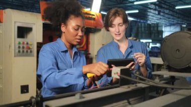 Güvenlik üniformalı iki profesyonel kadın mühendis, makinelerin voltaj akımını kontrol ederek, kontrol ederek ve imalat fabrikasında, elektrik sistemi işlerinde çalışırlar..