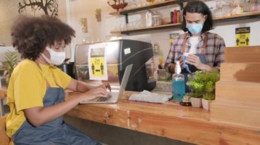 Kahve dükkanında yüz maskesi takmış iki genç kafe ortağı ve girişimci müşterilerin yeni normal yaşam tarzı hizmetinde sipariş vermelerini bekliyor. COVID19 salgınının KOBİ iş etkisini karantinaya alıyor..