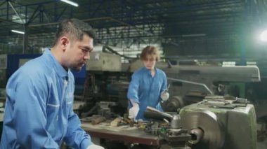 Profesyonel endüstri ekibi, güvenlik üniforması giyen iki işçi ve mühendis ortak metal iş aletleri, mekanik torna makineleri ve çelik fabrikasındaki yedek parça atölyesinde çalıştı..