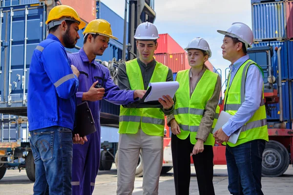A Group of multiracial workers people in safety uniforms and hardhats work at logistics terminal with many stacks of containers, loading control shipping goods for the cargo transportation industry.