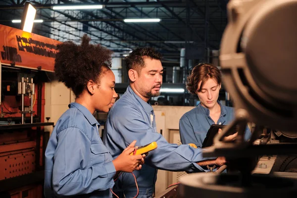 Multiracial professional industry engineer teams in safety uniforms work by inspecting machines\' voltage current, checking, and maintaining at manufacture factory, electric system service occupations.