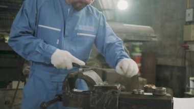 Profesyonel bir Asyalı erkek mühendis güvenlik üniforması içinde çalışıyor. Metal işçiliği hassas aletleri, mekanik torna makineleri ve çelik fabrikasında yedek parça atölyesi var..