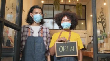 Yeni başlayan iki genç barista partneri, COVID-19 'dan sonra kafeterya işlerinde çalışırken maske takıp, mutlu ve neşeli gülümsemelerini takınıp, açık yazı yazıp, tabelayı gösteriyorlar..