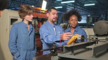 Güvenlik üniformalı çok ırklı profesyonel mühendislik ekipleri, makinelerin voltaj akımlarını kontrol ederek, kontrol ederek ve fabrikada, elektrik sistemi işlerinde çalışırlar..