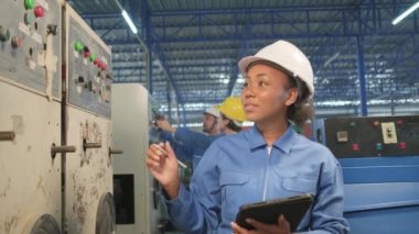 Professional African American female industry engineer in hard hat and safety uniform inspect machine's control panel, maintenance and check with tablet in manufacture factory, service occupation.