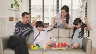 Happy Asian lovely Thai family care, dad, mum, and little children have fun playing with colorful toy blocks together on sofa in white living room, leisure weekend, and domestic wellbeing lifestyle.