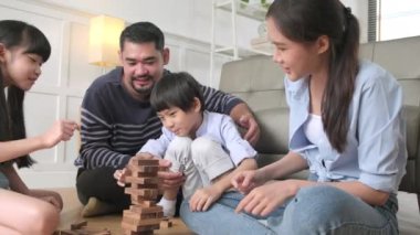 Happy Asian lovely Thai family activity, parents, dad, mum, and children have fun playing and joyful wooden toy blocks together on living room floor, leisure weekend, and domestic wellbeing lifestyle.