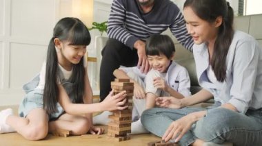 Happy Asian lovely Thai family activity, parents, dad, mum, and children have fun playing and joyful wooden toy blocks together on living room floor, leisure weekend, and domestic wellbeing lifestyle.
