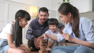 Happy Asian lovely Thai family activity, parents, dad, mum, and children have fun playing and joyful wooden toy blocks together on living room floor, leisure weekend, and domestic wellbeing lifestyle.