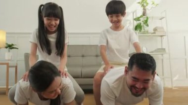 Happy well-being Asian Thai family, children play and tease their parents while yoga fitness training and health exercise together in the white living room, domestic home lifestyle, weekend activity.