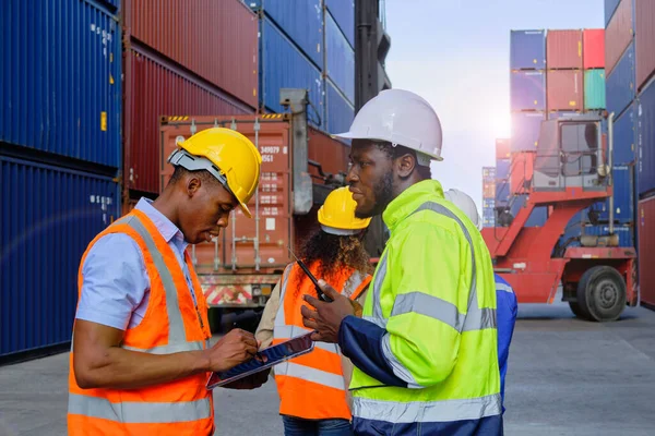 African American male workers and teams in safety uniforms and hardhats use walkie-talkies, work at logistic crane with stacks of containers, load control shipping goods, and cargo transport industry.