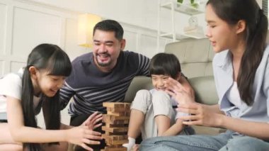 Happy Asian lovely Thai family activity, parents, dad, mum, and children have fun playing and joyful wooden toy blocks together on living room floor, leisure weekend, and domestic wellbeing lifestyle.