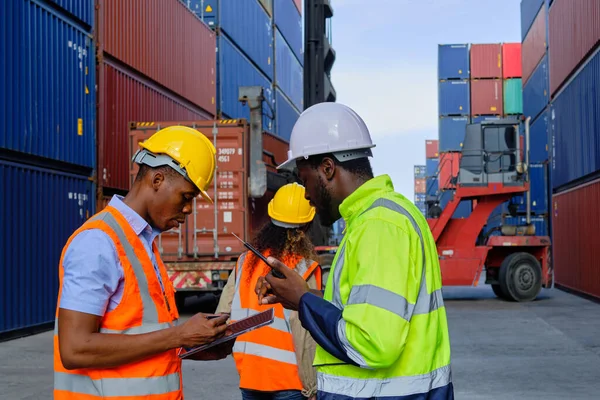 African American male workers and teams in safety uniforms and hardhats use walkie-talkies, work at logistic crane with stacks of containers, load control shipping goods, and cargo transport industry.