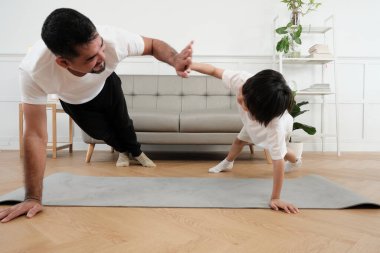 Young Asian Thai father lovely trains her little son to exercise and practices yoga on living room floor together for healthy fitness and wellness, happy domestic home lifestyle on family weekends.