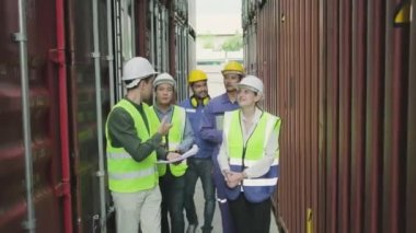 Group of multiracial workers in safety uniforms and hardhats walk and inspect shipping cargo with White male manager at nook of container stack, import and export goods logistic transport industry. 