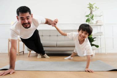 Young Asian Thai father lovely trains her little son to exercise and practices yoga on living room floor together for healthy fitness and wellness, happy domestic home lifestyle on family weekends.