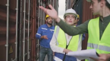 Group of multiracial workers in safety uniforms and hardhats walk and inspect shipping cargo with White male manager at nook of container stack, import and export goods logistic transport industry. 