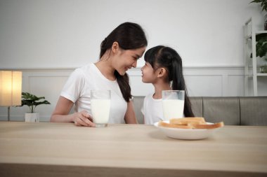 Sağlıklı Asya Tayland ailesi, mutlu küçük kız ve genç anne yemek masasında birlikte taze süt ve ekmekle birlikte, sağlıklı beslenme kahvaltısı, sabah yaşam tarzı.