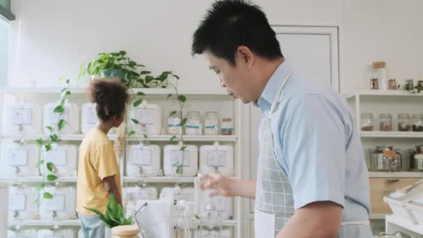 Asian Male Shopkeeper Works Laptop Checks Purchase Order Customer Chooses — Stock Video