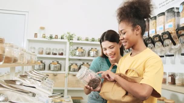 2人の若い女性の顧客は 再利用可能なバッグ 廃棄物ゼロの食料品 プラスチックフリー 環境に優しい持続可能なライフスタイルを補充店で有機製品を選択して買い物をしています — ストック動画