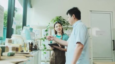 Kadın bir dükkan sahibi, mağazadaki Asyalı erkeklere doğal organik ürünler, sıfır atık ve plastiksiz bakkal, çevre dostu, sürdürülebilir yaşam tarzları ve yeniden kullanılabilir bir dükkan tanımlıyor..