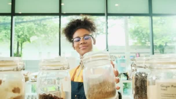 若い黒の女性店主は リフィル店 廃棄物ゼロ プラスチックフリー食料品店 環境に優しい小売業で再利用可能な容器に天然有機製品のガラス瓶をきれいにする — ストック動画