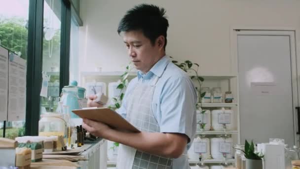 Asian Male Shopkeeper Checks Stock Natural Organic Products Window Display — Vídeo de Stock